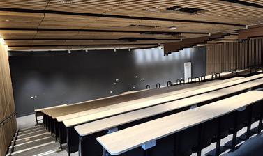 View of the basement lecture theatre of the Life and Mind Building, nearly completed, with wooden desks and panelling and a black front wall