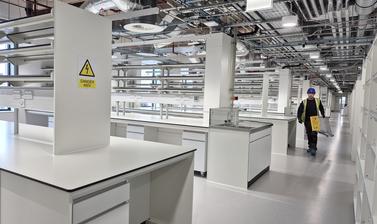 A construction worker wearing PPE, carrying a safety ladder through an empty laboratory space in the Life and Mind Building, featuring banks of white lab desks and tiered shelving
