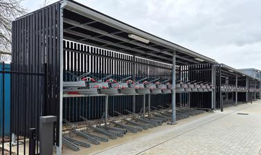 New covered metal cycle storage units outside the Life and Mind Building, beside a paved walkway, on a cloudy spring day
