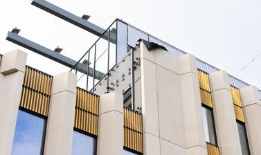 Vew of outside of the upper floors of the Life and Mind Building, looking up towards the roof, with two long metal girders exposed to the top-left