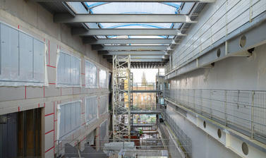 View down an empty atrium within the building, with skylight roof and the eye drawn to Oxford spires in the background