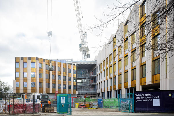 View of emerging entrance to Life and Mind Building (exterior), on a cloudy November day, with a construction crane in the background and security fencing in the foreground